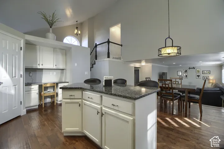 Open-concept living area featuring high vaulted ceilings, wood-finish flooring, a kitchen island with stone-finish countertop, and a built-in desk area with cabinetry