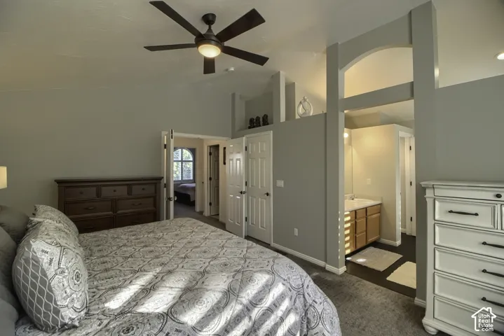 Vaulted ceiling with a ceiling fan, arched doorway, and an integrated vanity with a wood-finish cabinet and white sink