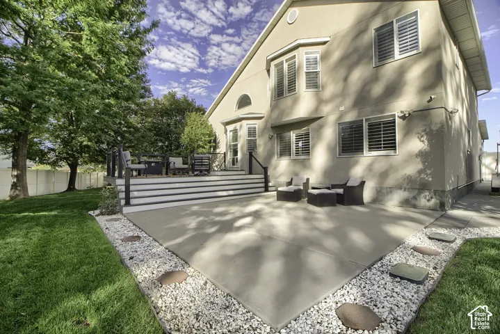 Expansive rear concrete patio, elevated composite deck, manicured lawn, and mature trees