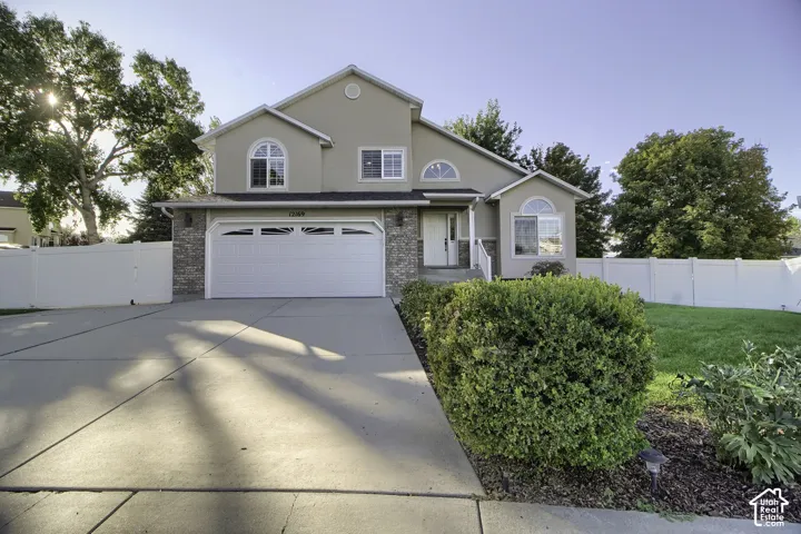 Stucco exterior with stone accents, two-car garage, concrete driveway, arched windows, and white perimeter fencing
