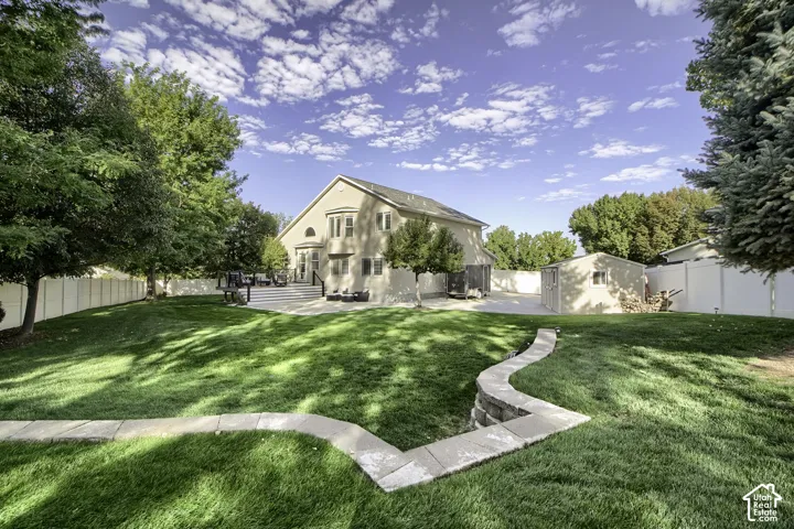 Expansive backyard featuring a manicured lawn, mature trees, a multi-level deck, and a detached storage shed