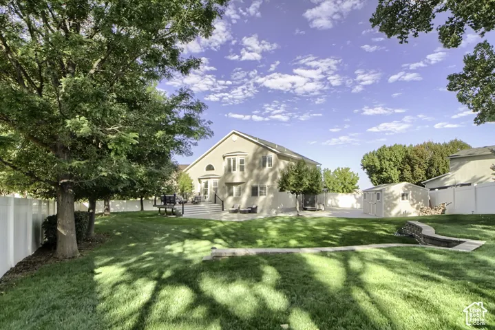 Expansive green lawn with mature trees, a multi-level deck, a privacy fence, and an outdoor storage shed