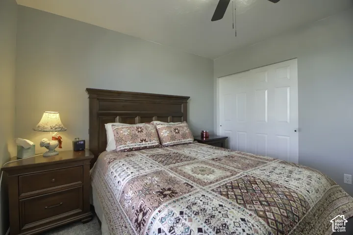 Wood-finish headboard, built-in closet with panel doors, ceiling fan, and light gray wall paint