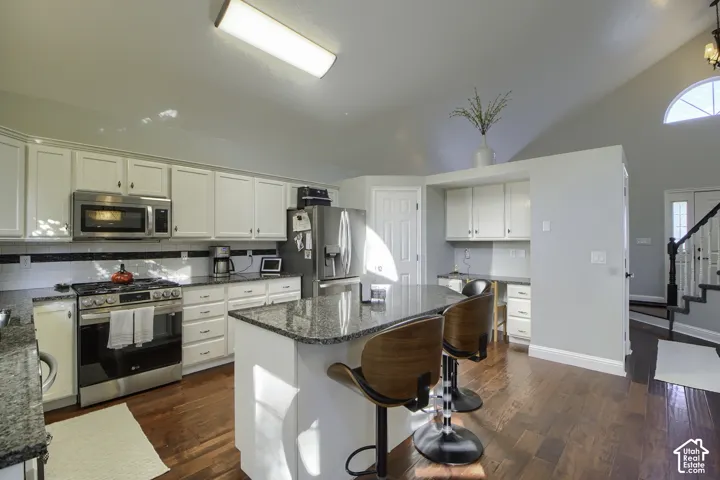 Kitchen featuring white cabinetry, stainless steel appliances, granite countertops, wood-finish flooring, and a vaulted ceiling