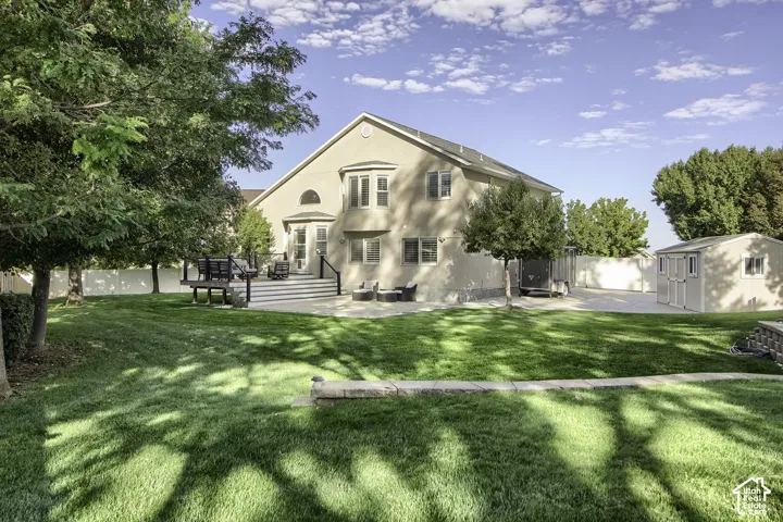 Expansive backyard featuring a manicured lawn, a multi-level deck, a concrete patio, a detached storage shed, and mature trees