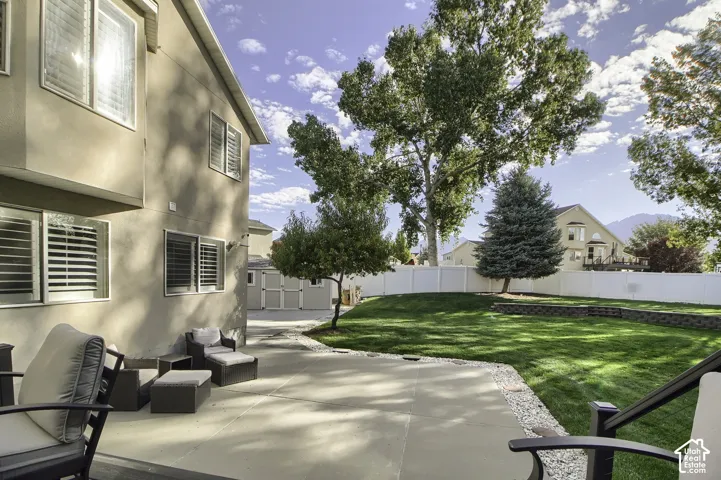 Expansive concrete patio with a privacy fence, manicured lawn, and mature trees