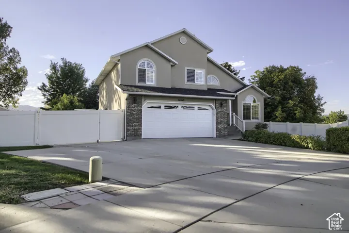 Two-story stucco exterior featuring stone accents, an attached two-car garage, and a gated perimeter fence