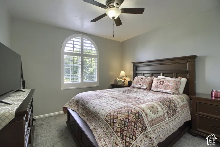 Arched window with plantation shutters, ceiling fan with integrated lighting, wood-finish headboard, coordinating wood-finish nightstands