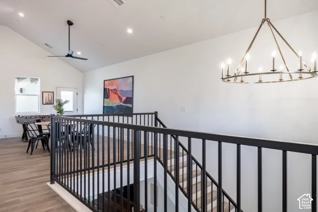 Vaulted ceiling with recessed lighting, wood-finish flooring, black metal stair railing, and a rustic chandelier