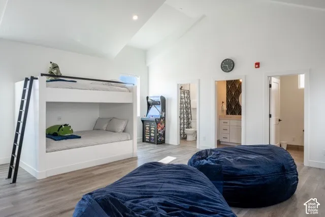 White bunk bed with a ladder, wood-finish flooring, vaulted ceiling, and recessed lighting