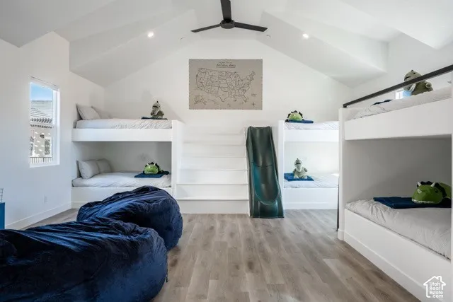 Vaulted white ceilings, built-in bunk beds, window with white trim, wood-finish flooring, and a ceiling fan with light