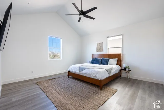 Vaulted ceiling with a ceiling fan, plank flooring, and multiple windows