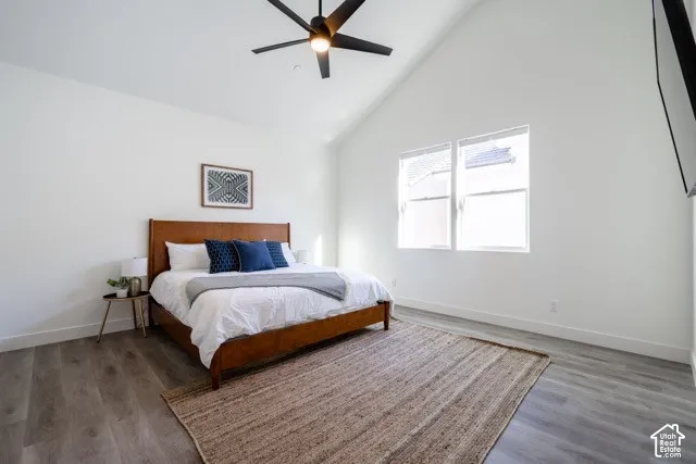 Vaulted ceiling with a ceiling fan, two windows, wood-finish flooring, and white walls