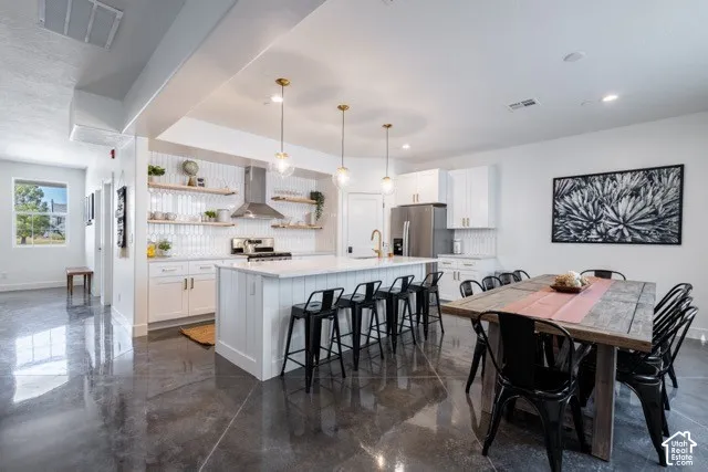 Open-concept kitchen featuring an island with counter seating, stainless steel appliances, white cabinetry, and floating wood-finish shelves
