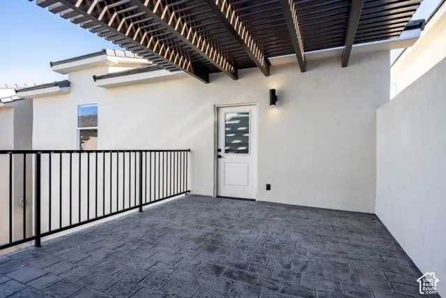 Patio with stamped concrete flooring, a decorative wooden pergola, and black metal railing
