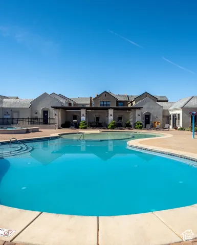 Curved swimming pool, concrete pool deck, attached spa, covered patio, and stucco building exteriors