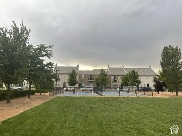 Expansive green lawn with mature trees and a dedicated sports court, bordered by a black metal fence