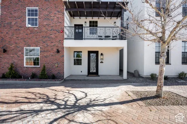 Brick and stucco exterior, second-story balcony with iron railing, paver driveway, and decorative entry door