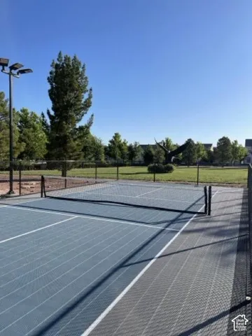 Fenced multi-sport court with blue and gray modular surfacing, court lighting, and a net