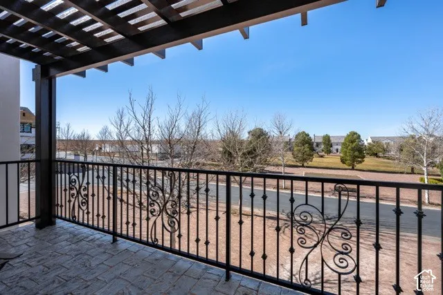 Elevated outdoor living space featuring a decorative wrought-iron railing, paver terrace, and pergola overhead