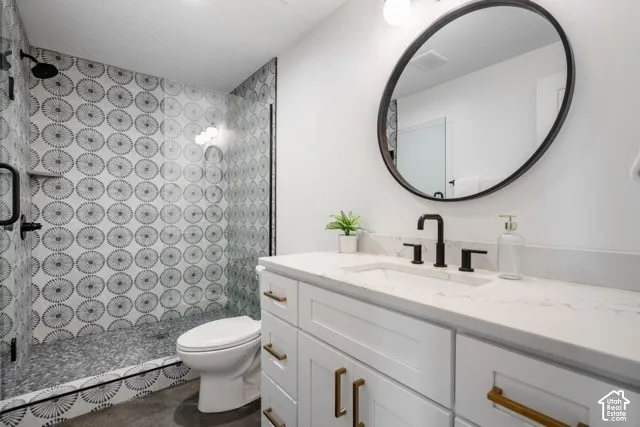 Contemporary bathroom featuring a walk-in shower with patterned wall tile and pebble floor, a white vanity with gold-tone hardware, a white countertop with an integrated sink, and a black-framed oval mirror