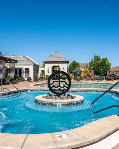 Heated pool area with a circular spa, stone-tile coping, and a decorative metal art feature