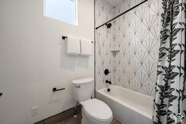 Bathtub with black fixtures, decorative tiled shower surround, and a compact toilet