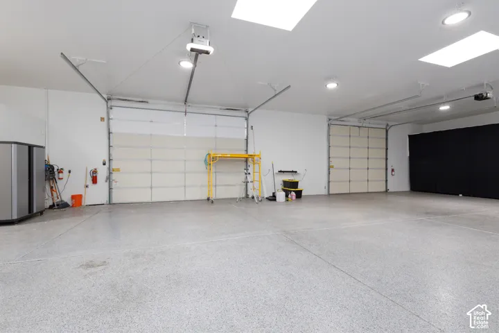 Spacious garage featuring epoxy-coated flooring, dual overhead doors with automatic openers, recessed and pendant lighting throughout, a yellow gantry crane system, and ample storage infrastructure