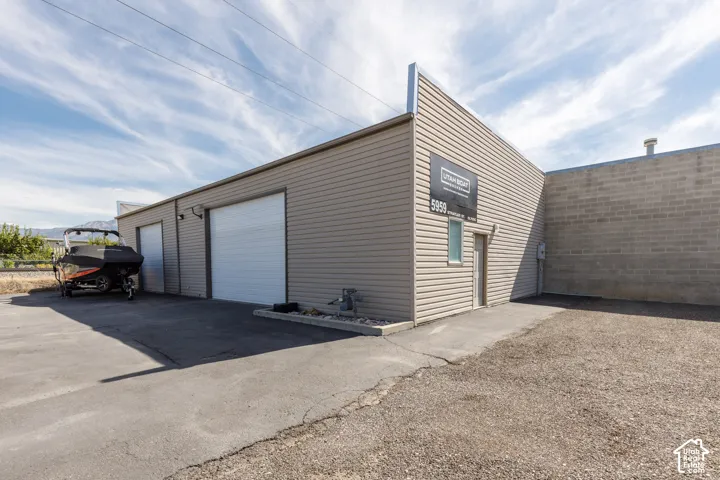 Commercial building with two roll-up doors, a pedestrian entrance, light tan horizontal siding, and a partial concrete block exterior