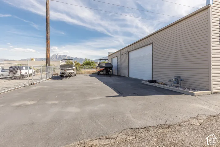 Metal-sided building with multiple white roll-up doors, paved lot, and chain-link fencing