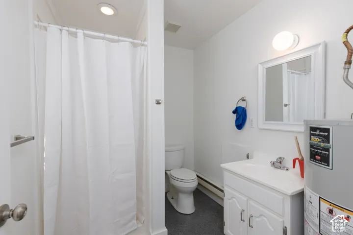 Recessed lighting, baseboard heating, white vanity with integrated sink, wall-mounted mirror, and a water heater