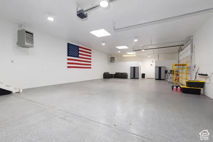Expansive garage with epoxy-coated concrete flooring, multiple overhead lighting fixtures, and a wall-mounted heater