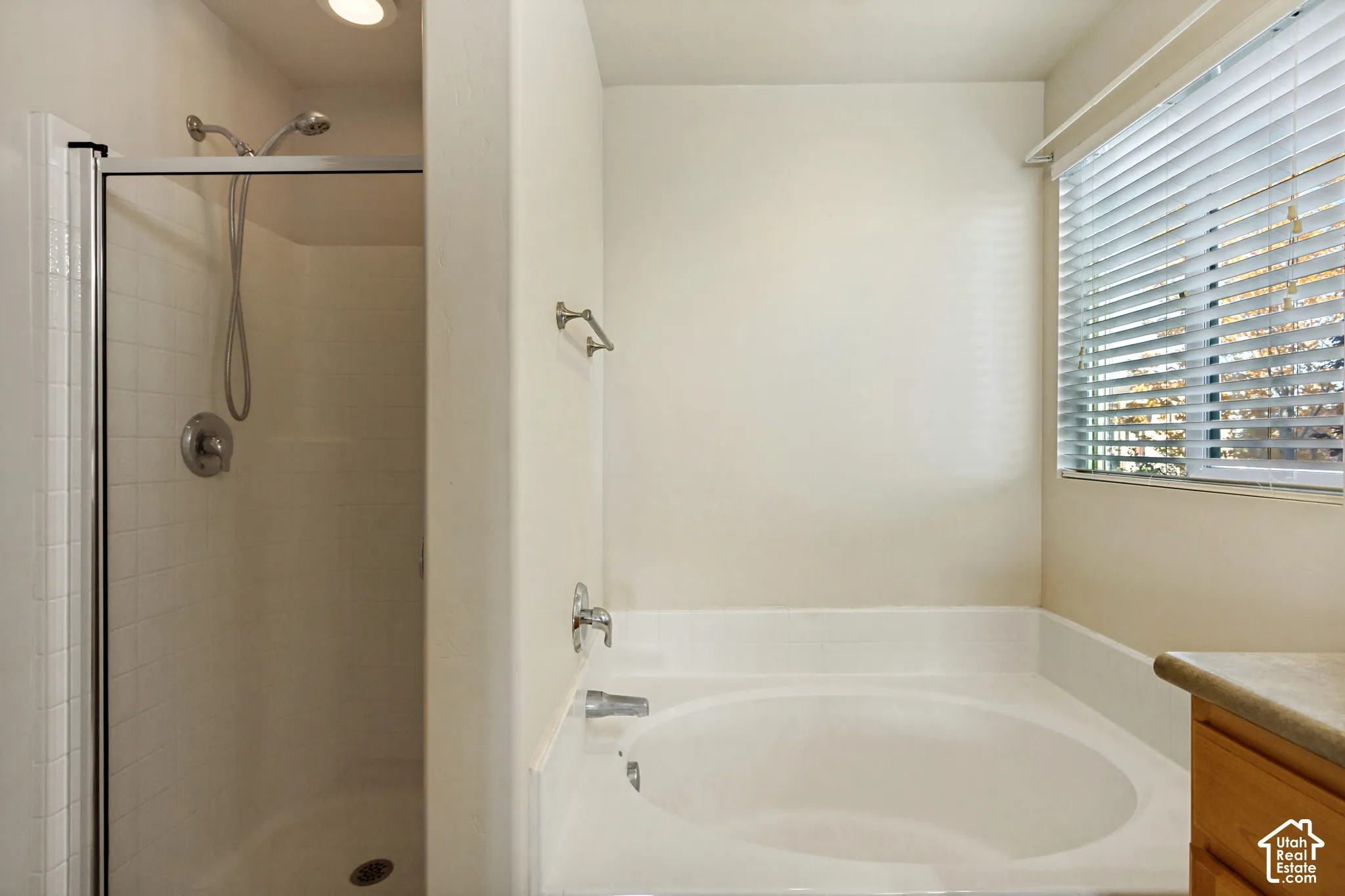 Step-in shower with clear glass enclosure, recessed lighting, built-in soaking tub with deck-mounted faucet, and a window with blinds