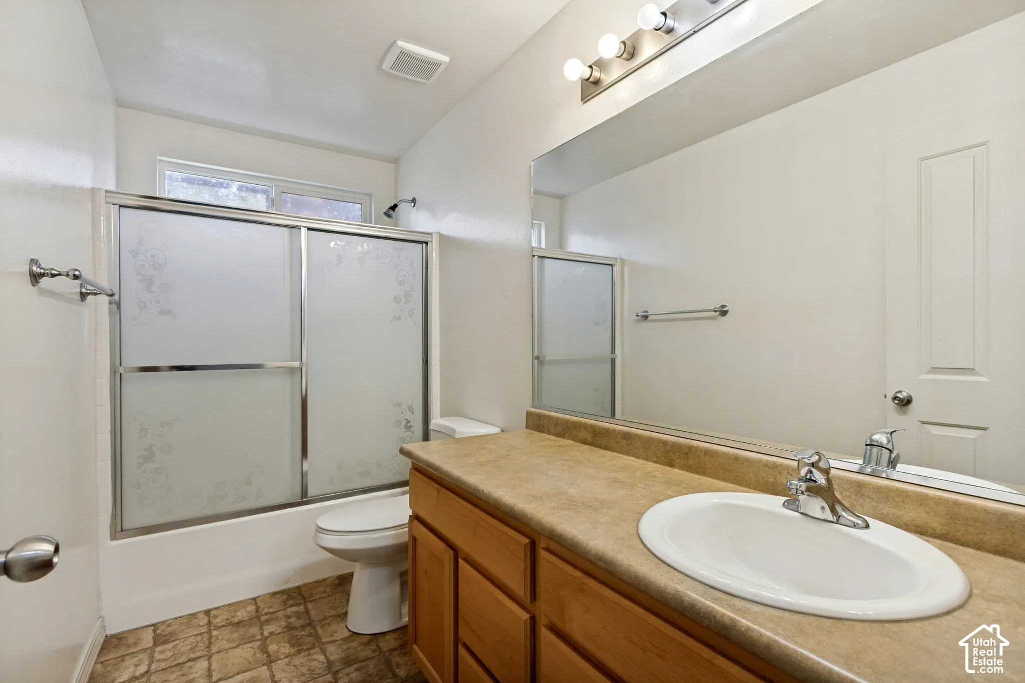 Bathroom featuring a wood-finish vanity with an integrated sink, a large mirror, and a shower-tub combination with frosted glass doors
