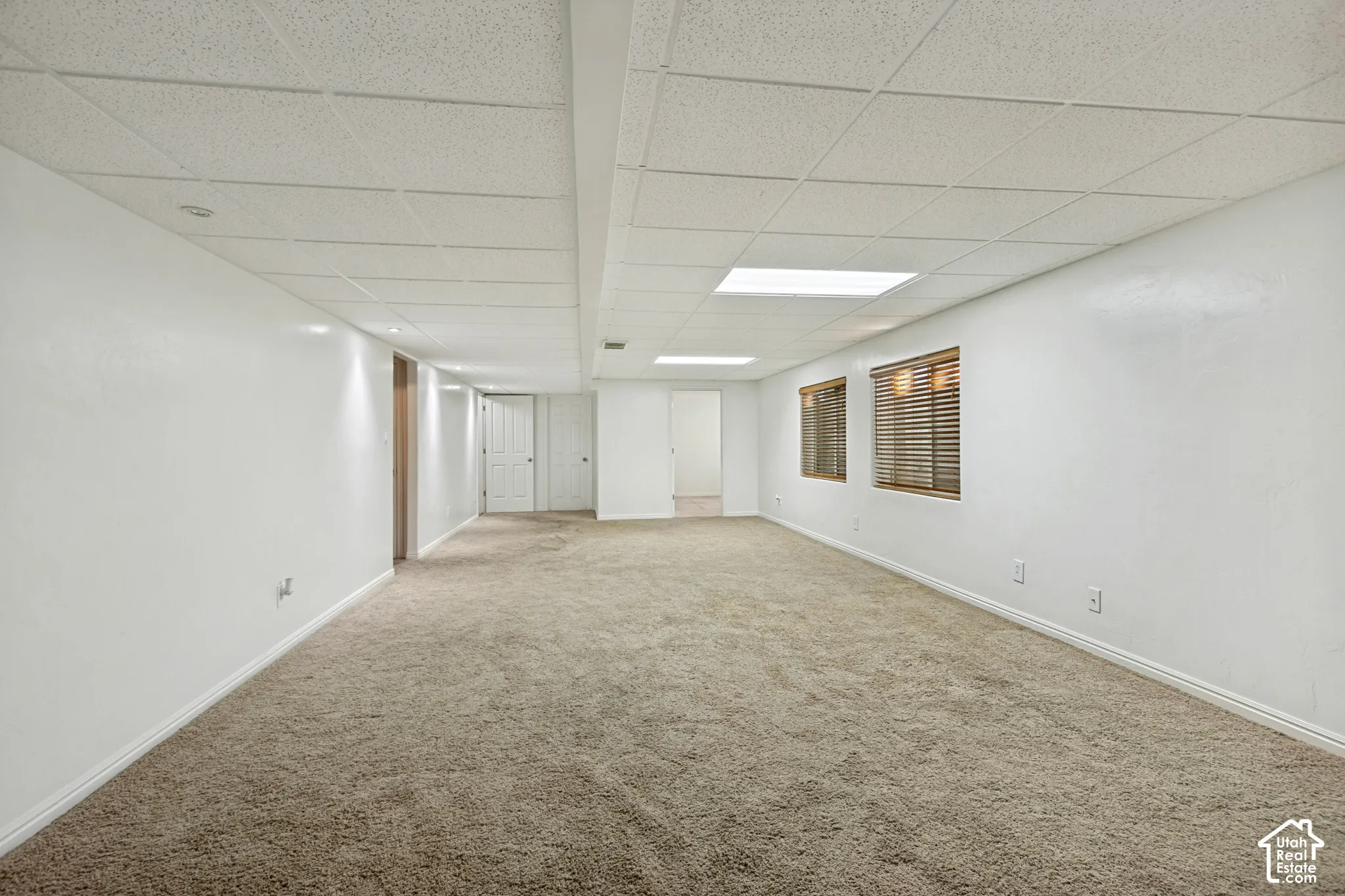 Expansive carpeted area with white walls and a drop ceiling