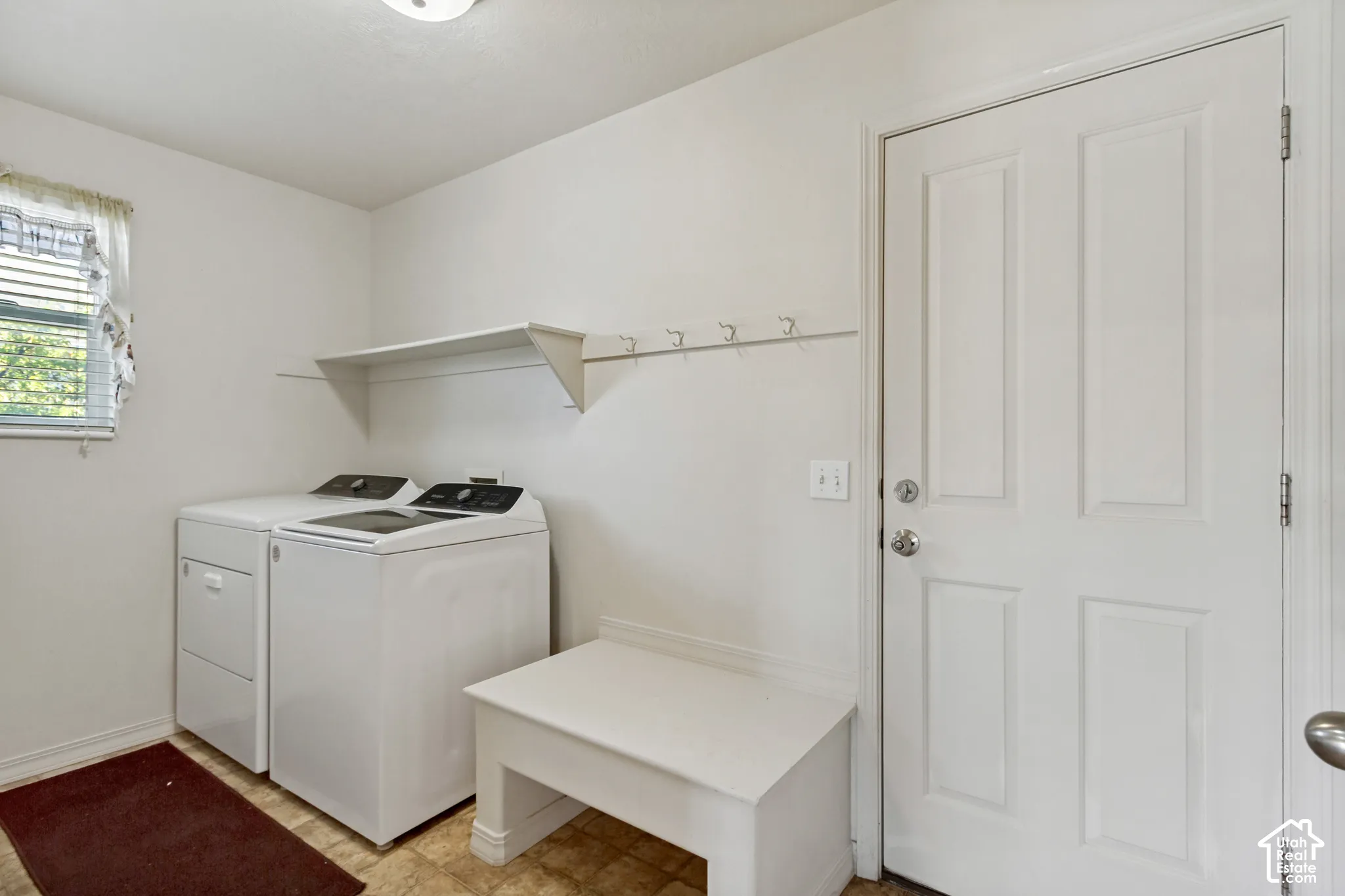 Laundry area featuring a window with blinds, a built-in storage shelf, a wall-mounted coat rack, and a paneled entry door