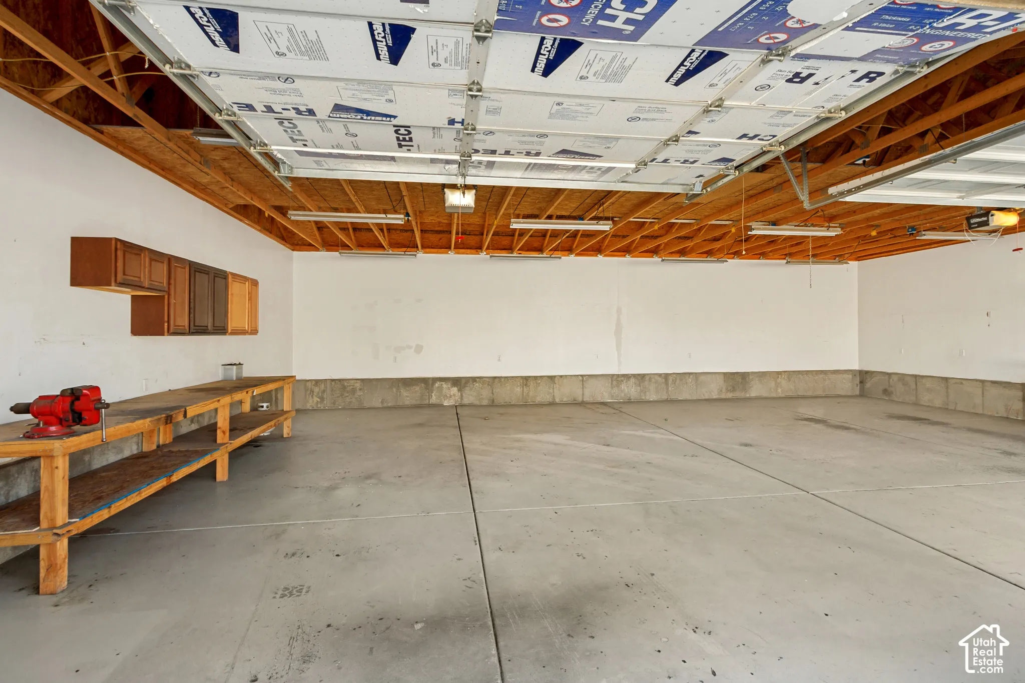 Concrete flooring, exposed wood ceiling joists, overhead lighting, built-in wall cabinets, and an integrated workbench