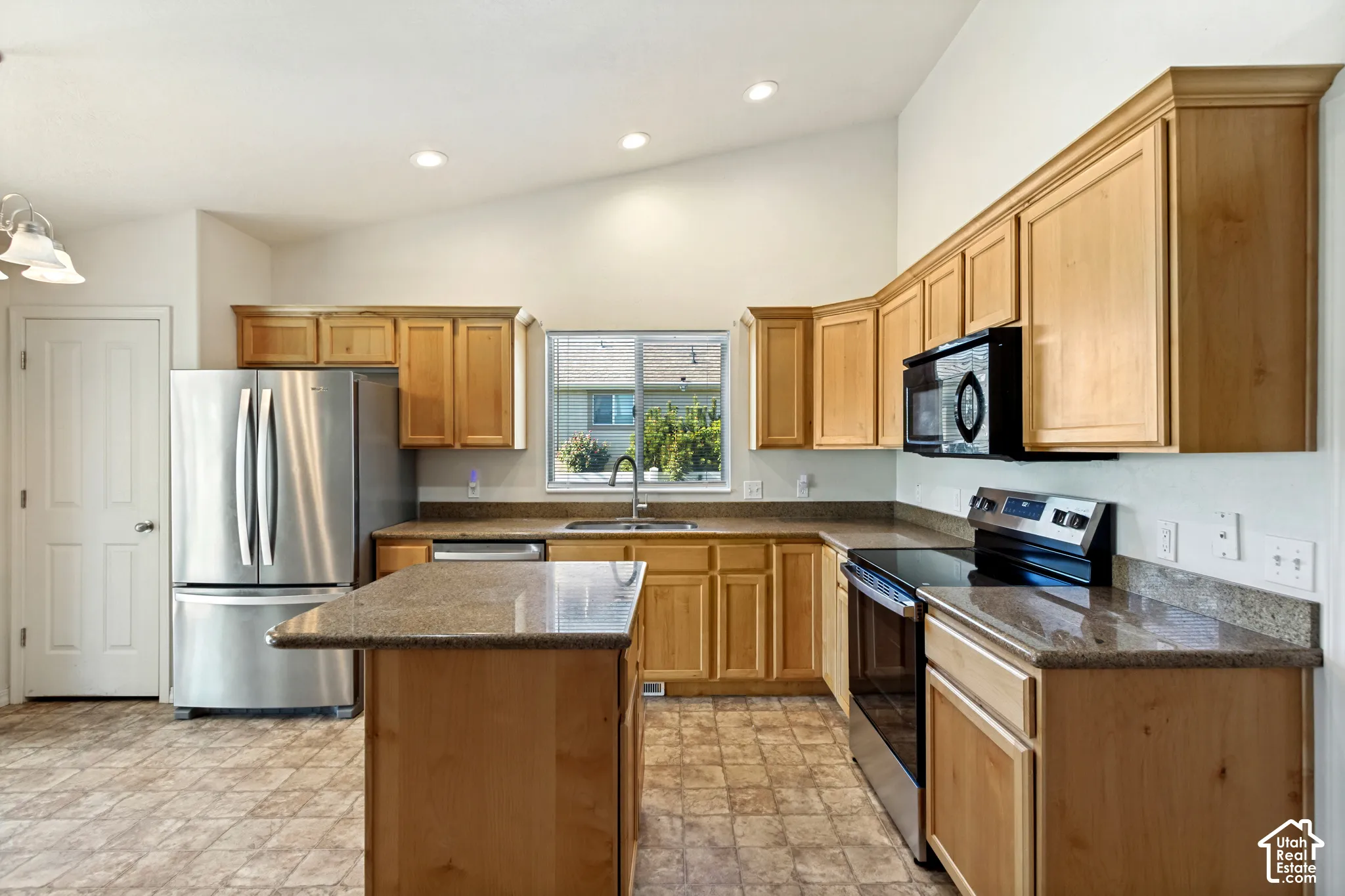 Kitchen featuring light wood cabinetry, stone-finish countertops, stainless steel appliances, and an island with bar seating