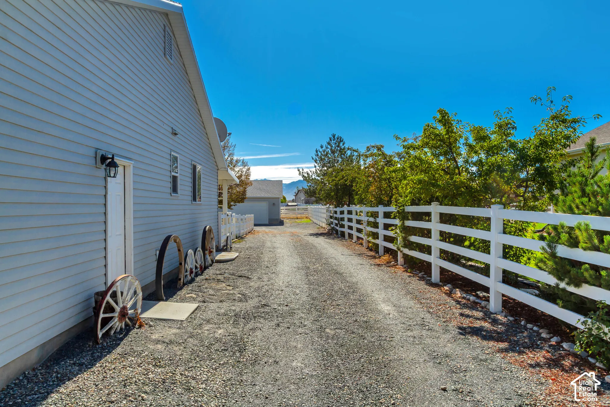 Gravel driveway with white fencing and mature landscaping