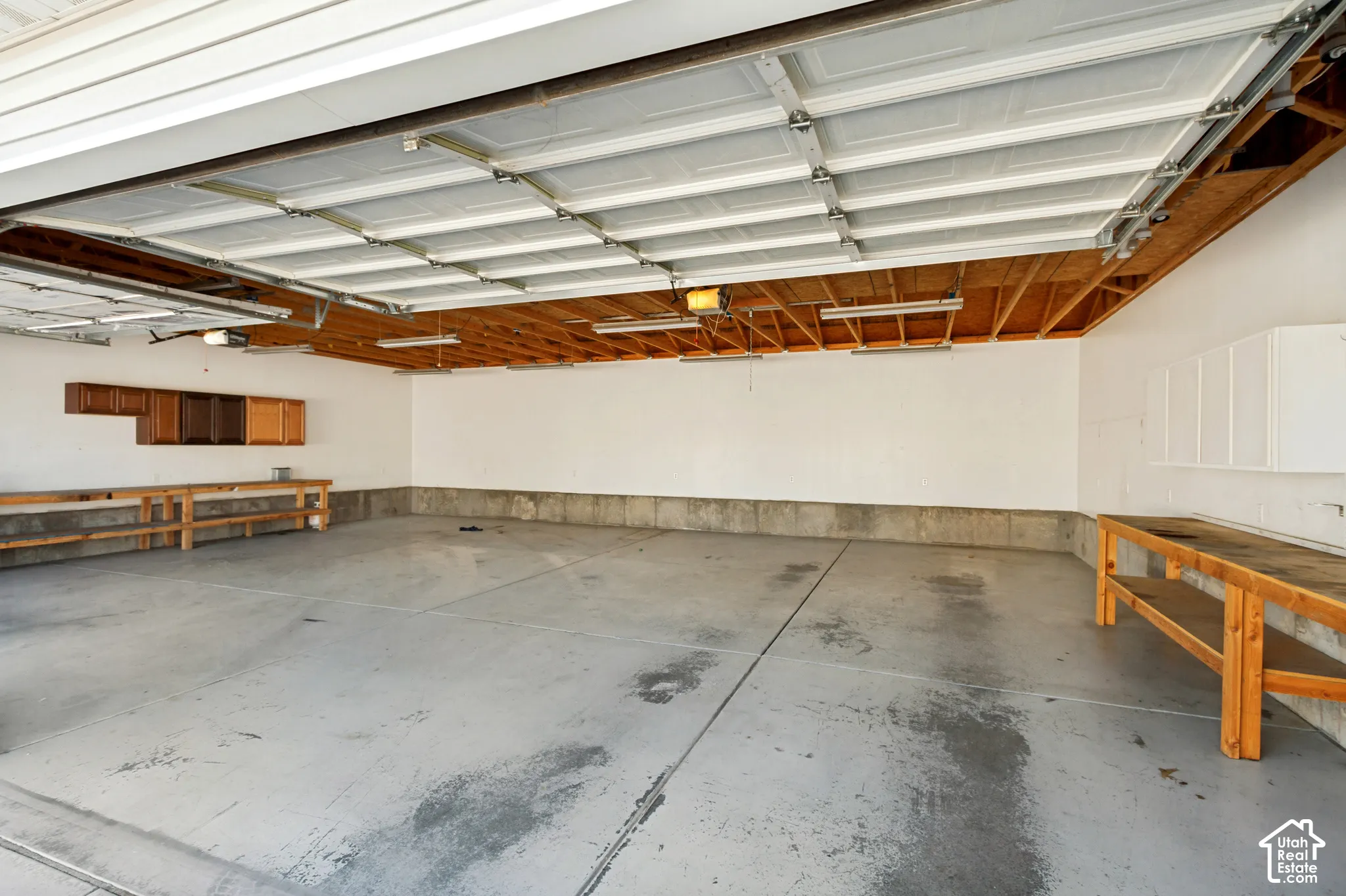 Spacious garage featuring a concrete floor, built-in wooden workbenches, overhead lighting, and wall-mounted cabinetry