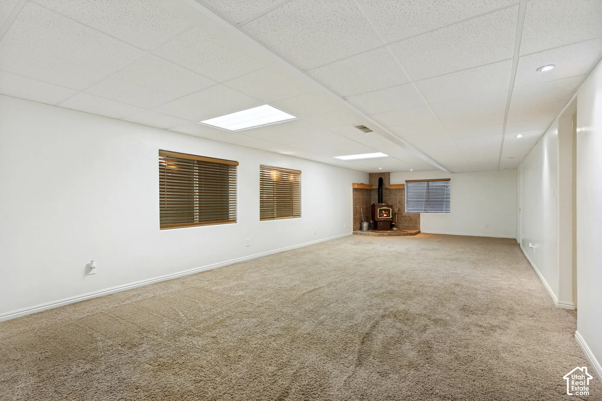 Open-concept living space with plush carpet flooring, recessed lighting, and a corner wood-burning stove with a stone surround
