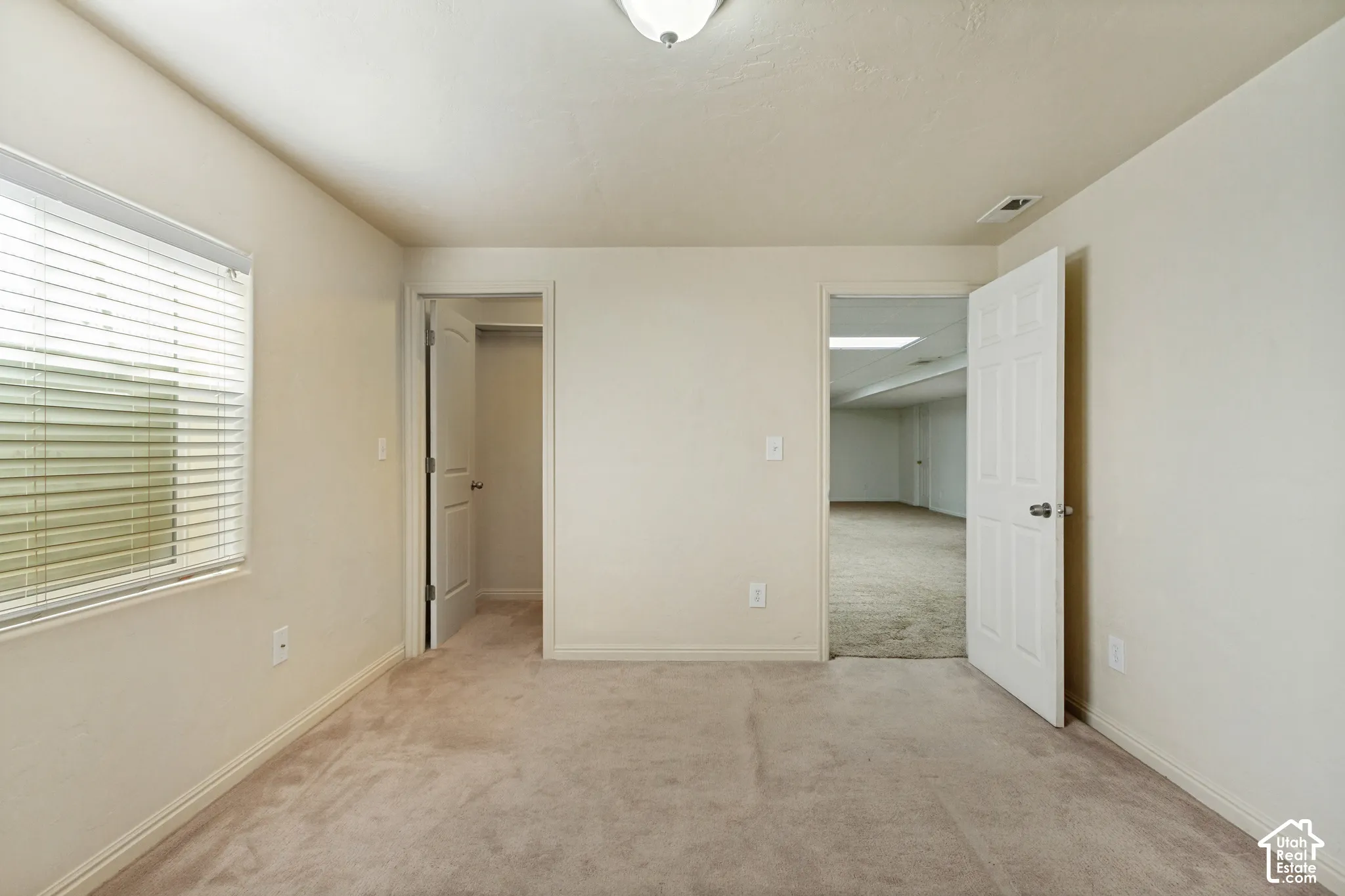 Carpeted flooring, window with horizontal blinds, overhead lighting, and white interior doors