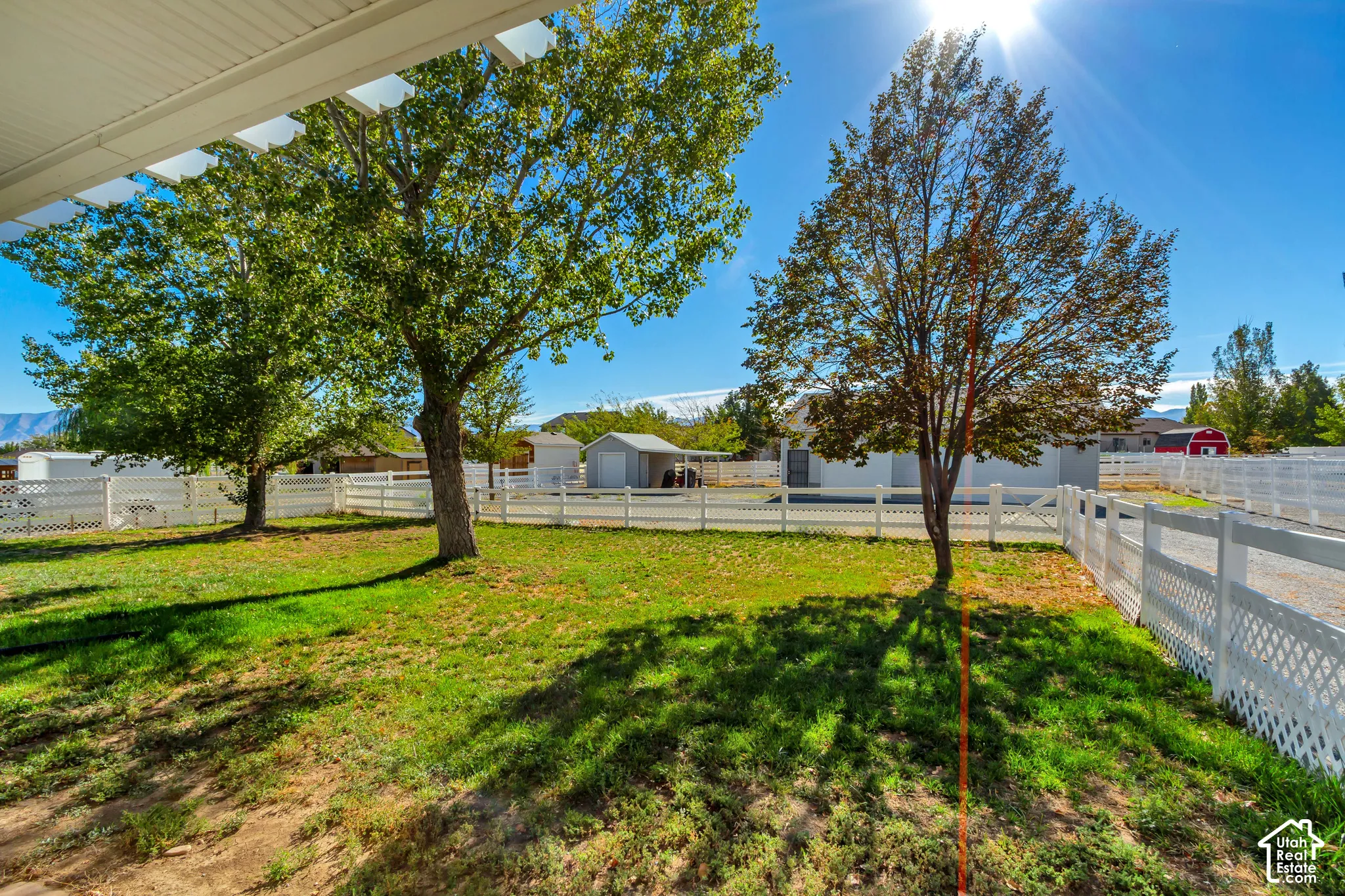 Expansive yard featuring mature trees, white lattice fencing, and a gravel driveway