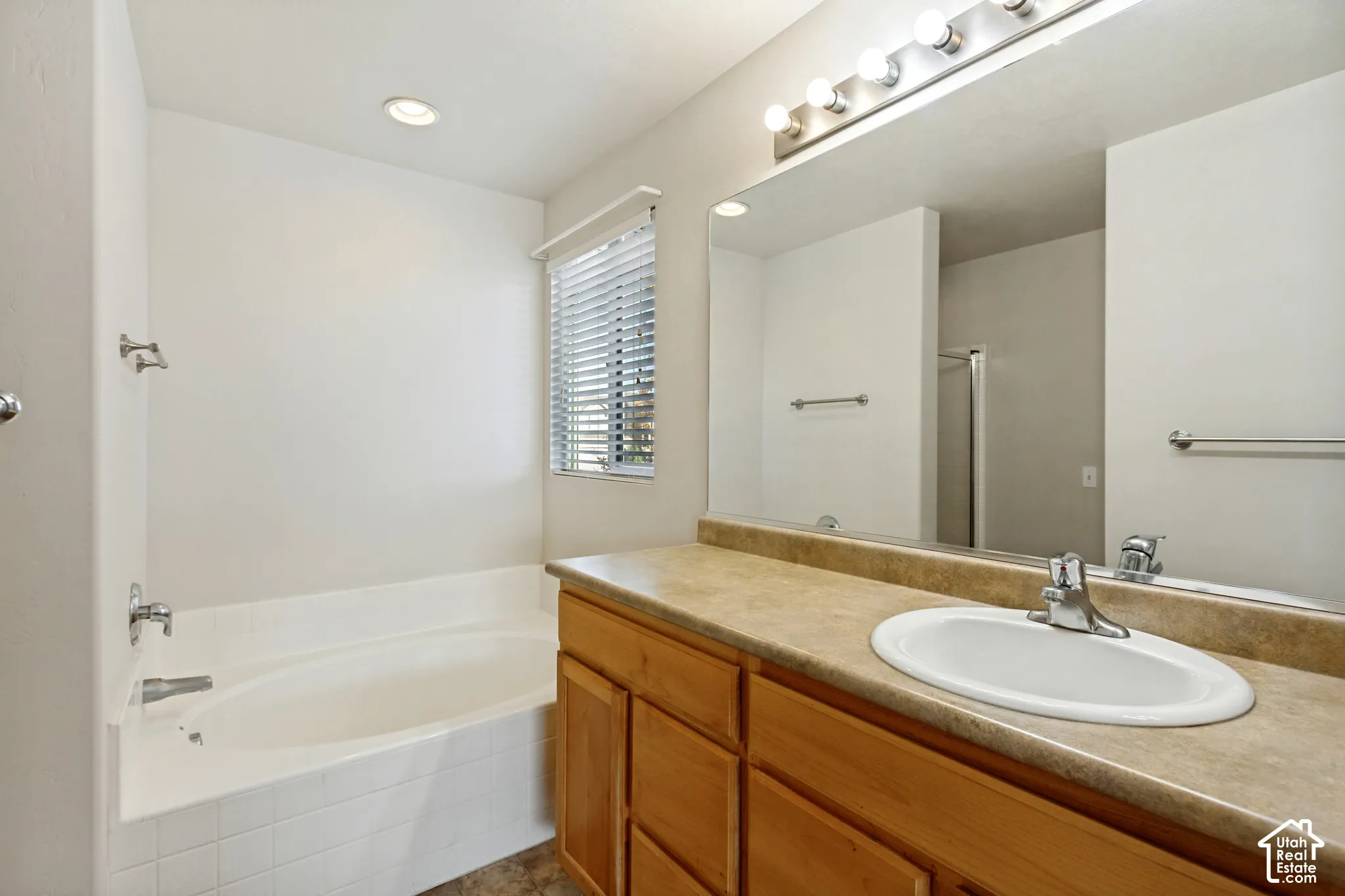 Recessed lighting, wood-finish cabinetry, built-in bathtub, and a vanity light fixture