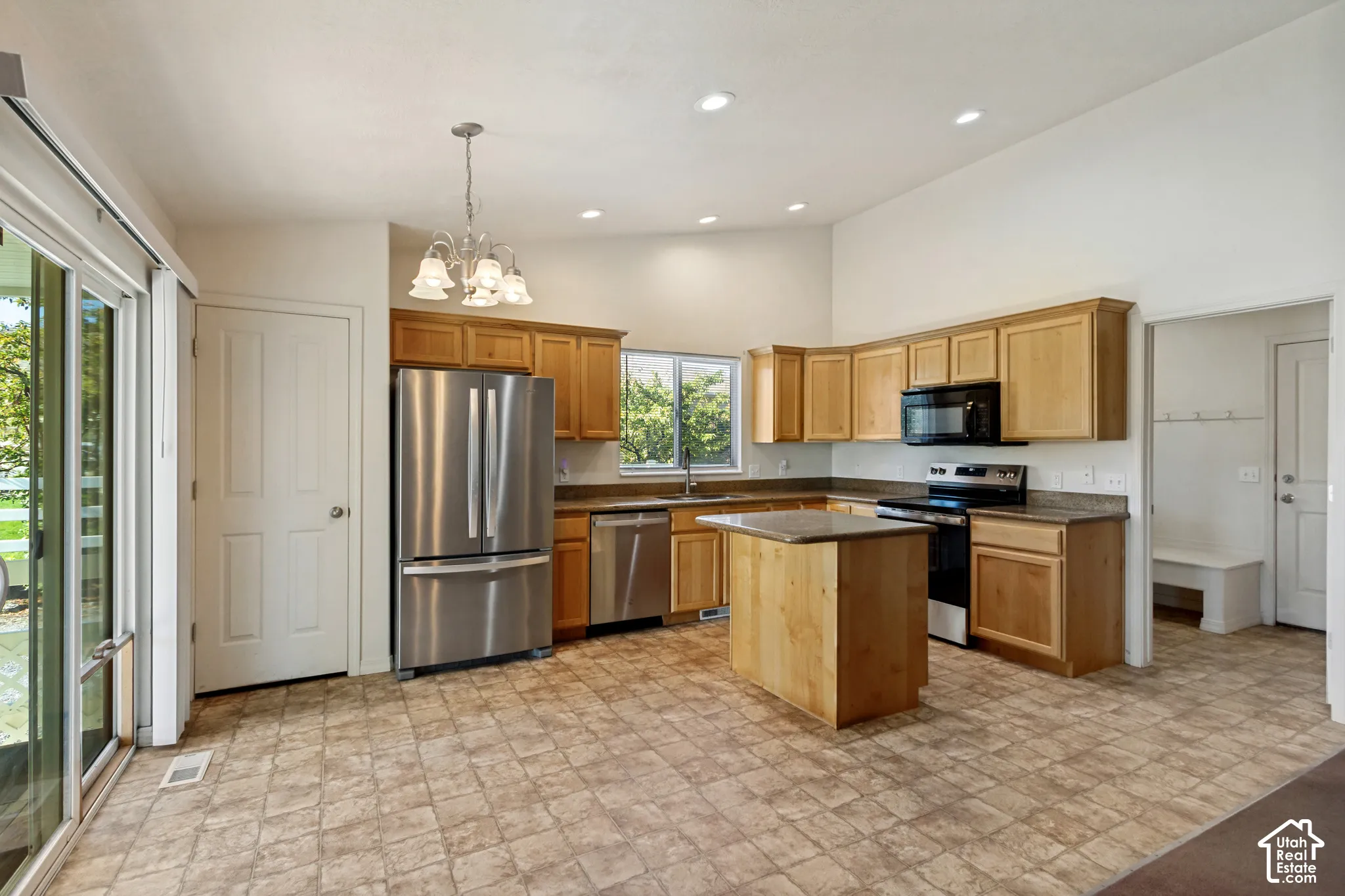 Spacious kitchen featuring wood-finish cabinetry, stainless steel appliances including a French-door refrigerator and electric range, tile flooring, a center island with seating space, recessed lighting, and abundant natural light from multiple windows