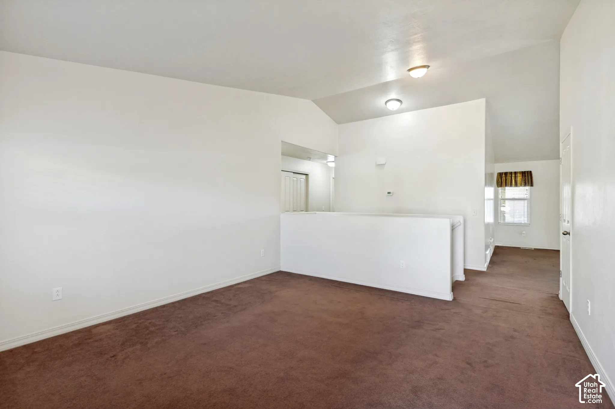 Vaulted ceilings with flush-mount lighting, brown carpet flooring, and a half-wall partition