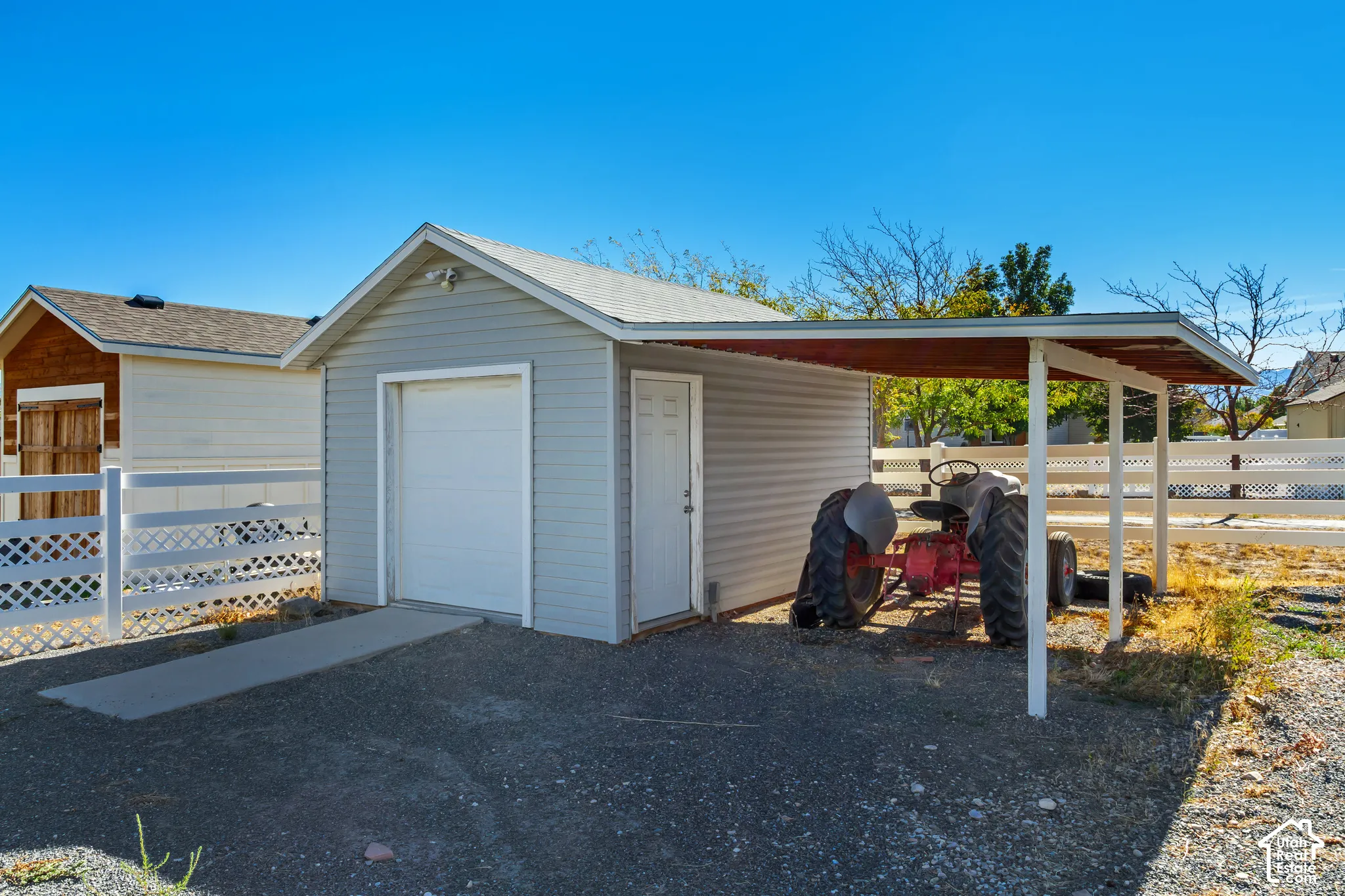 Detached garage with a roll-up door, an exterior side door, and a tractor that is included.