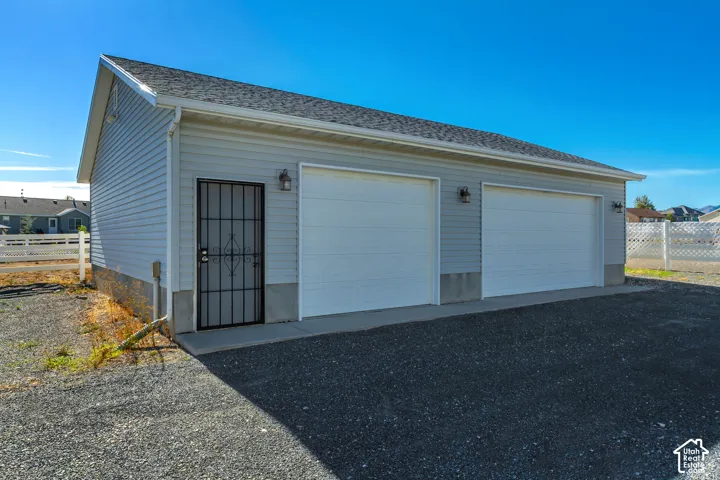 Detached structure featuring light gray siding, a dark shingle roof, two garage doors, and an additional entry door with a security screen