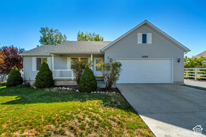 Charming ranch-style home featuring a front-facing two-car garage, covered front porch with decorative railings, and manicured landscaping with mature evergreen plantings