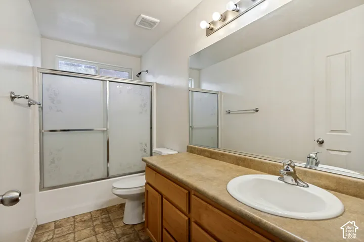 Bathroom featuring a wood-finish vanity with an integrated sink, a large mirror, and a shower-tub combination with frosted glass doors